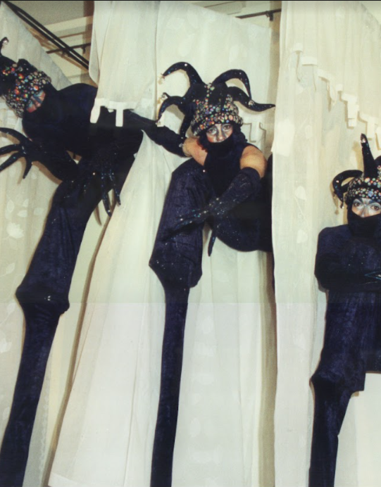 Three performers in elaborate black costumes on stilts