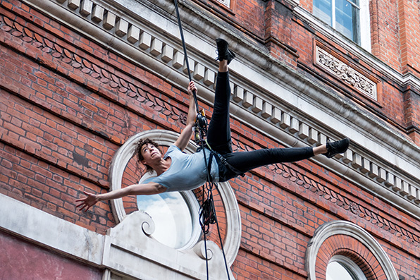 Performer suspended mid-air in front of red brick building