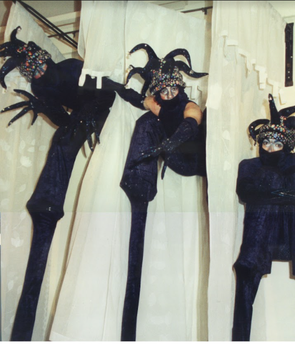 Three performers in elaborate black costumes on stilts