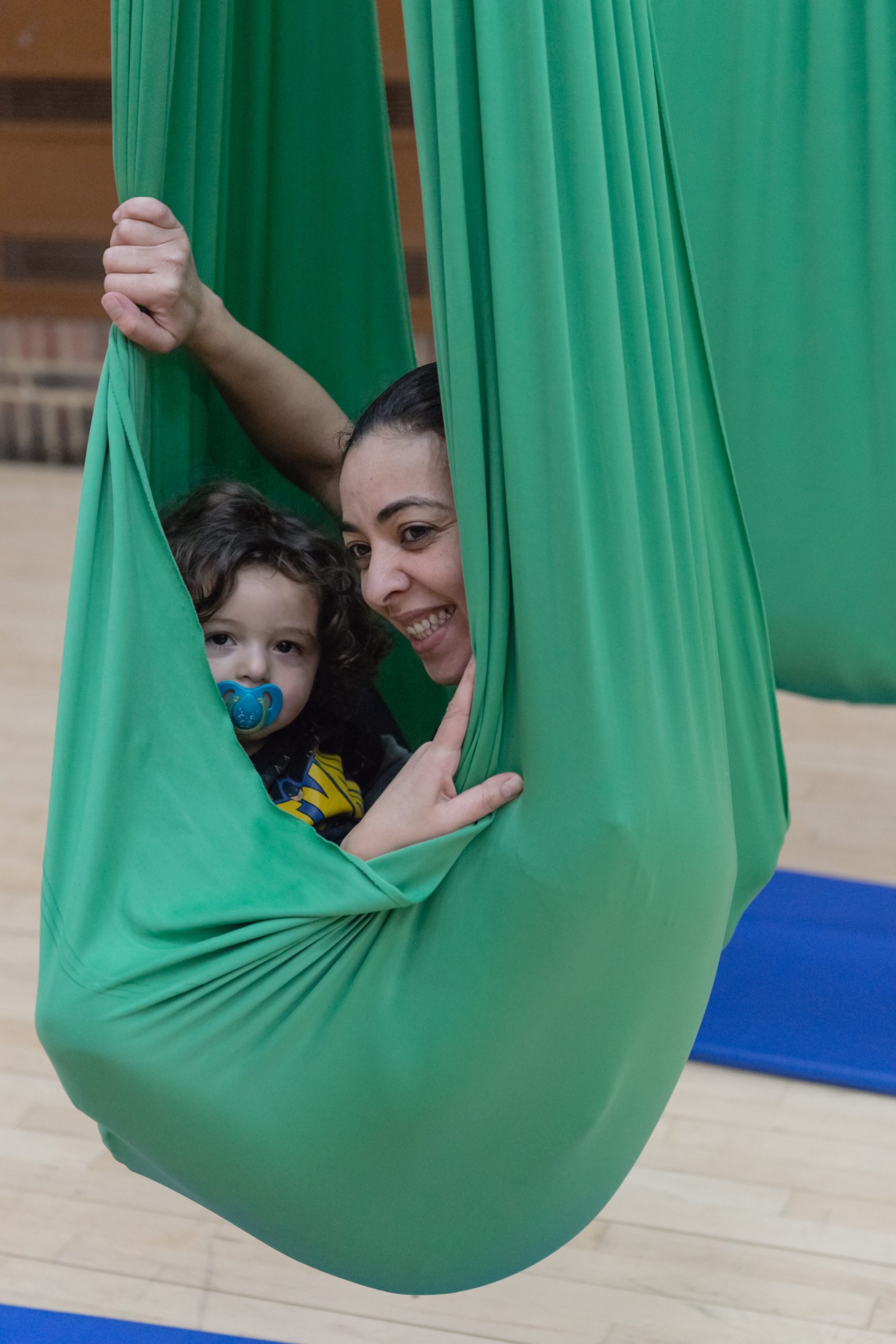 A mother and child peek out from a green cocoon, smiling to the photographer.