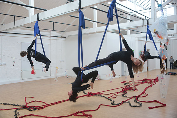 Group of women in different poses suspended on blue aerial silk.