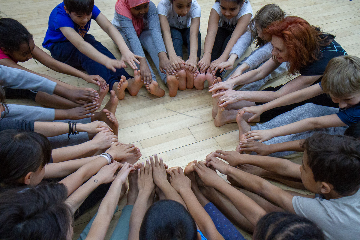 Photograph of Founder Daniela Essart with group of children sitting in circle reaching for their toes