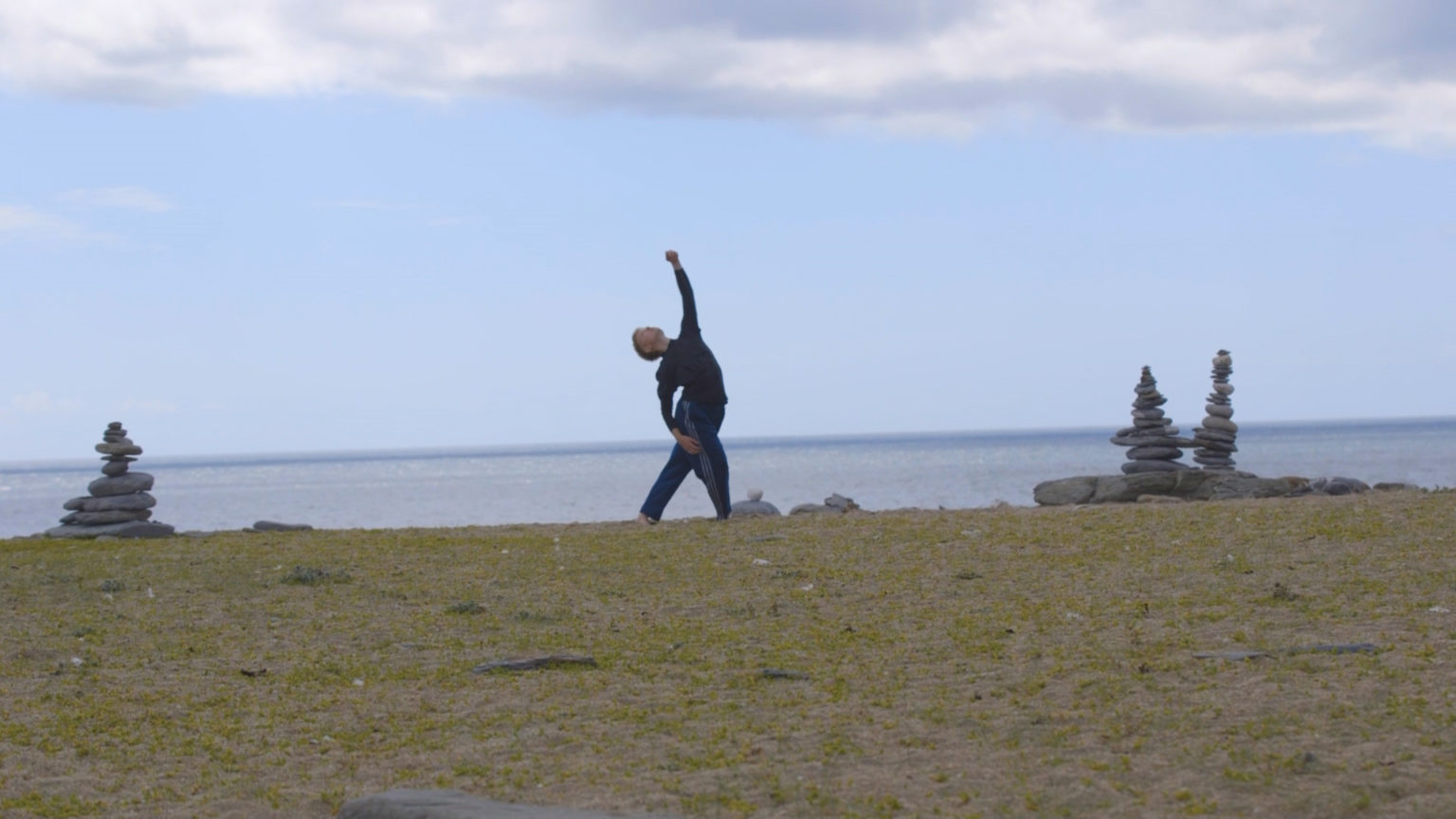 Person reaching to the sky with sea in the background, dancing on the beach.