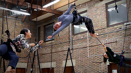 Three performers suspended by rope in studio space